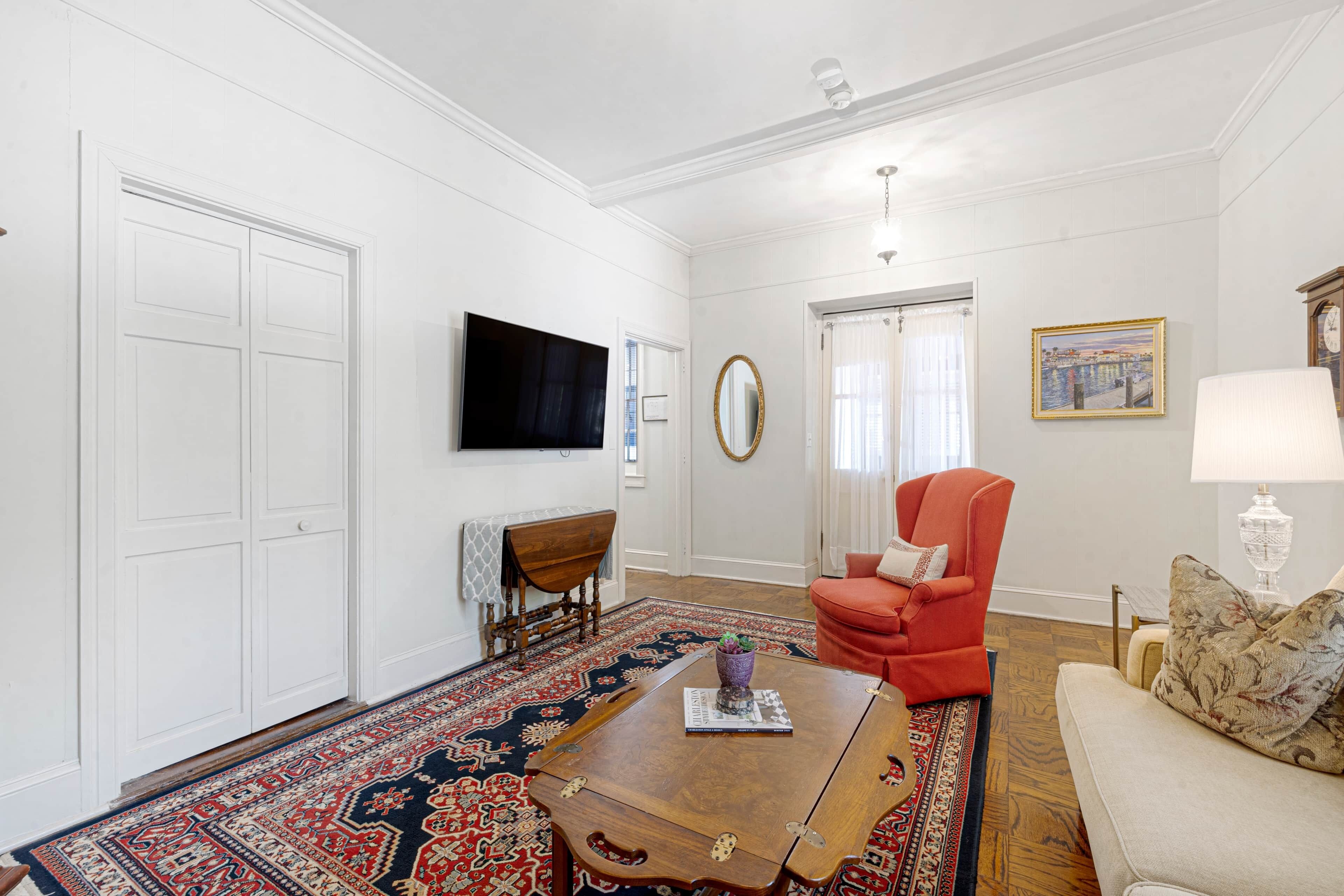 A living room with a large wooden coffee table, a red armchair, a beige sofa, a television, and a patterned rug.