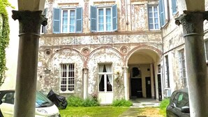 A courtyard with a building featuring arched doorways and columns, surrounded by parked cars and a grassy area. - "La Dama alla Finestra," charming apartment in the historic center of Como. (Como)