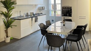 A modern kitchen with white cabinets, a dining table with chairs, a potted plant, and a large window. - "La Dama alla Finestra," charming apartment in the historic center of Como. (Como)
