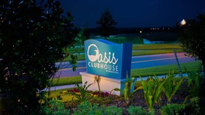 A sign for Oasis Clubhouse at ChampionsGate, surrounded by landscaped greenery and a well-maintained lawn. - Ohana Memories At Championsgate (Davenport)