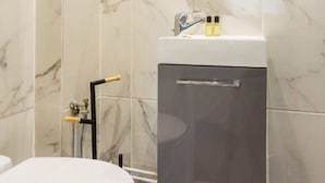A bathroom with a white toilet, a sink with a mirror above it, and a trash bin. - Cosy Studio, 1 chambre, Père Lachaise, Place de la nation (Paris)