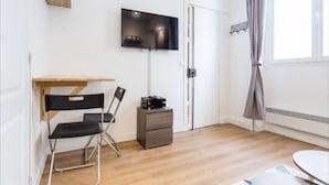 A compact room with a foldable desk, a chair, a television mounted on the wall, and a small cabinet. - Cosy Studio, 1 chambre, Père Lachaise, Place de la nation (Paris)