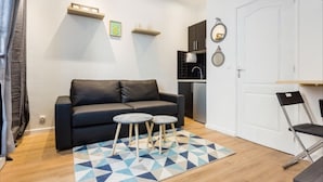 A modern living room with a black sofa, two small round tables, and a geometric patterned rug. - Cosy Studio, 1 chambre, Père Lachaise, Place de la nation (Paris)