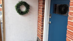 Una puerta blanca con el número 119, un adorno de flores verdes y una puerta azul con una ventana.
