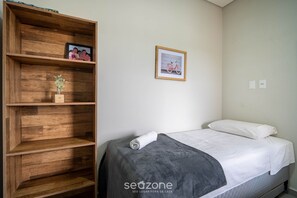 A bedroom with a bed, a wooden wardrobe, and a framed picture on the wall. - Apto moderno c/varanda em Campeche CRN101 (Florianópolis)