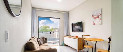 A modern living room with a sofa, a small table, a TV, and a balcony with a view of the city.
