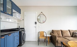A compact living space with a kitchenette, a sofa, a chair, and a round table. - Apto moderno c/varanda em Campeche CRN101 (Florianópolis)