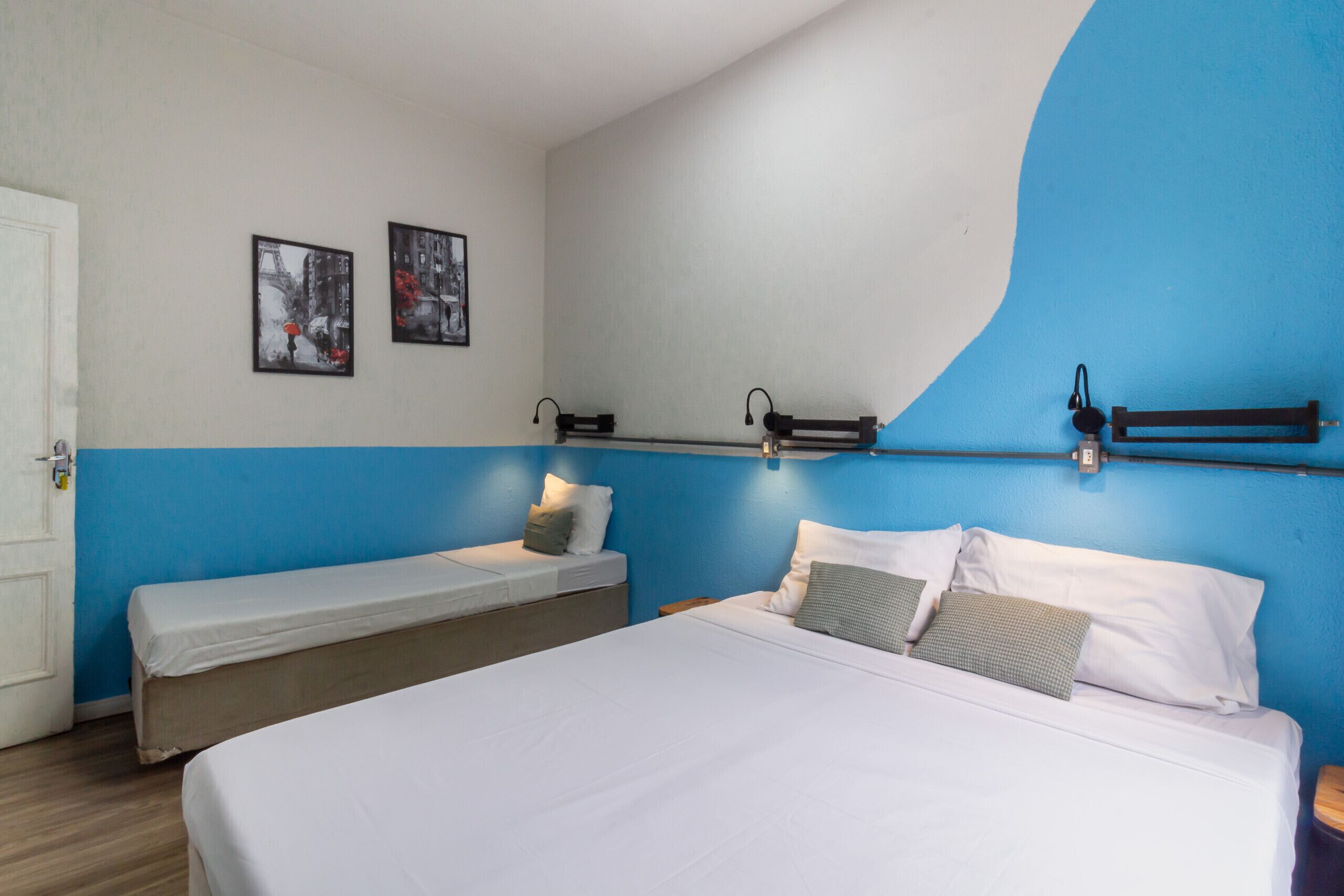 A hotel room with a large bed, a smaller bed, and a bench. There are two framed pictures on the wall.