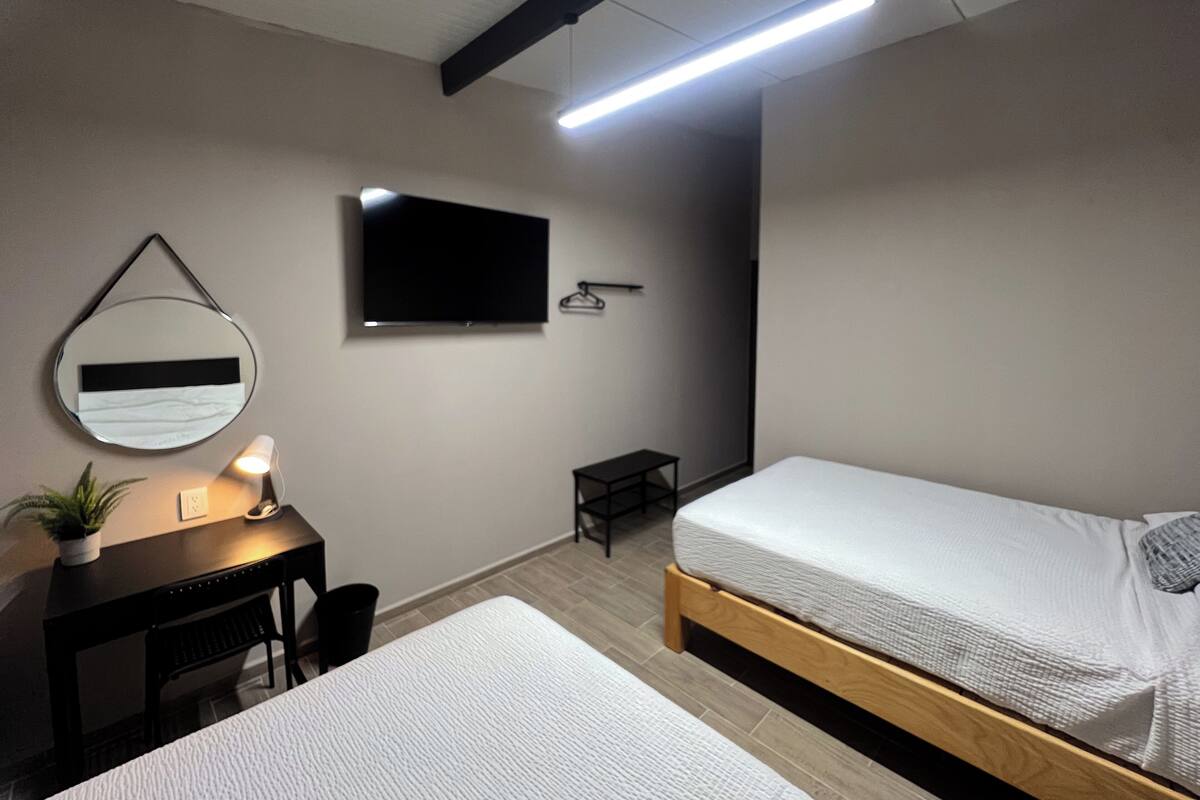 Ein Schlafzimmer mit Bett, Schreibtisch, Stuhl, Fernseher und Spiegel.