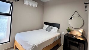 Ein Schlafzimmer mit einem Bett, einem Schreibtisch, einem Stuhl, einem Spiegel und einem Fenster.