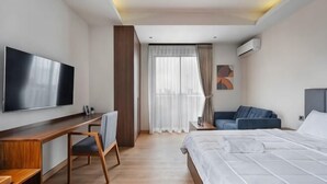 A hotel room with a bed, a desk, a chair, a TV, and a window with curtains. - Cove Amartha (South Jakarta)