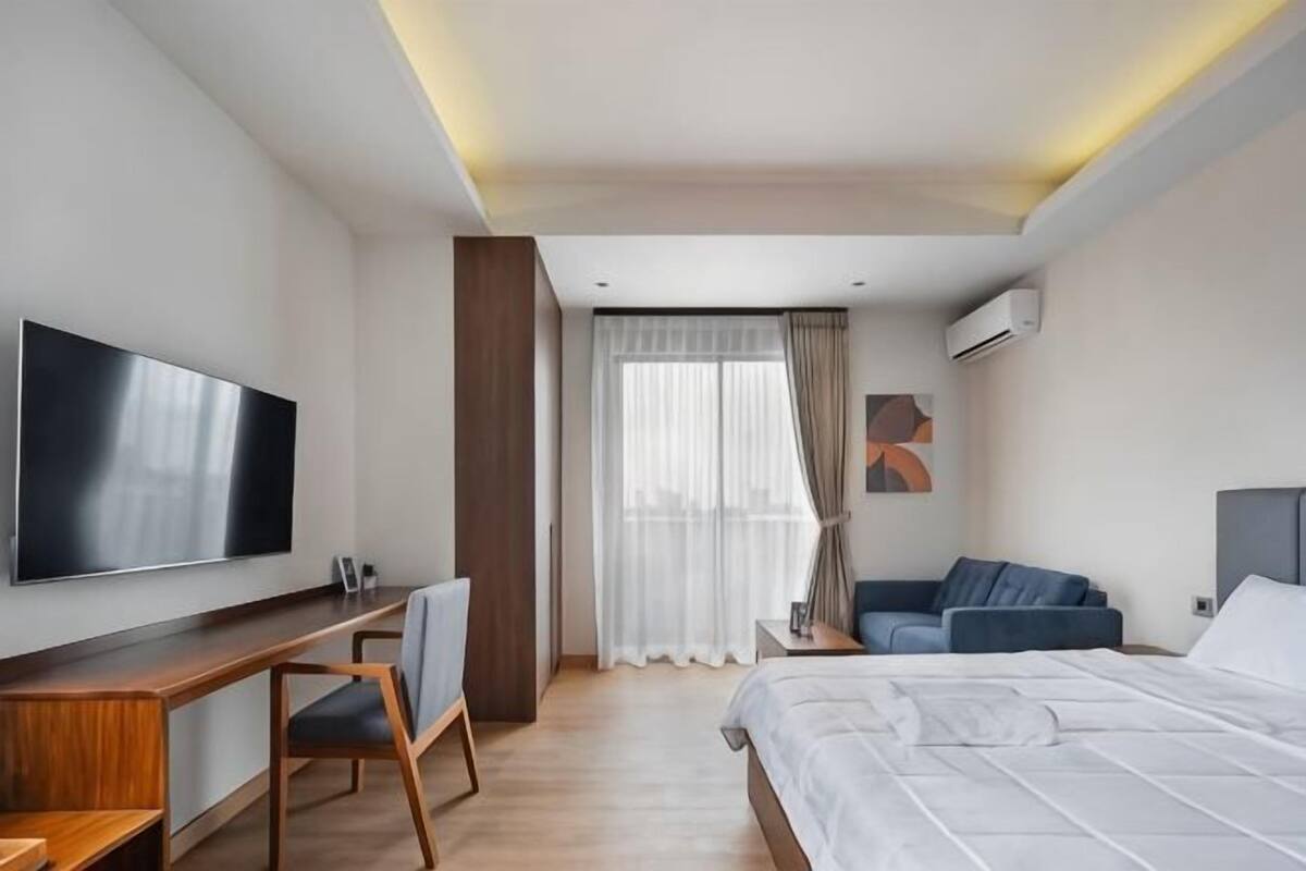 A hotel room with a bed, a desk, a chair, a TV, and a window with curtains.
