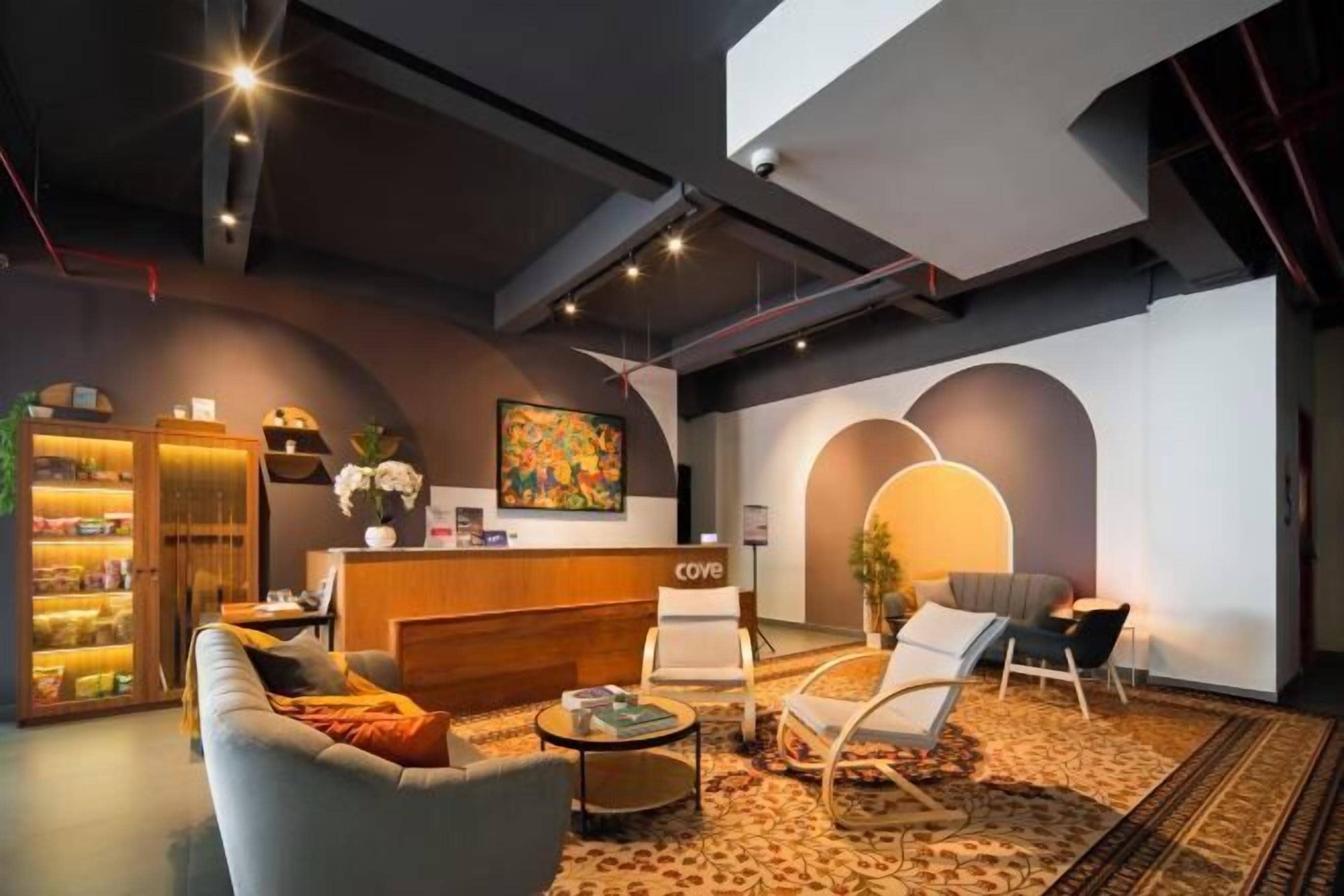 A modern hotel lobby with a reception desk, seating area, and a bookshelf.