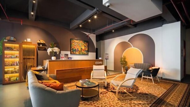 A modern hotel lobby with a reception desk, seating area, and a bookshelf. - Cove Amartha (South Jakarta)