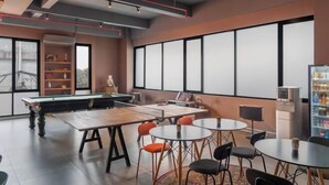 A modern lounge area with a pool table, multiple seating arrangements, and large windows providing natural light. - Cove Amartha (South Jakarta)