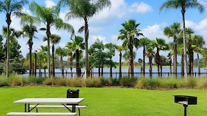 A picnic table and mailbox in a grassy area with a lake and tall trees in the background. - Modern 4BR Resort Townhome near Universal (Orlando)