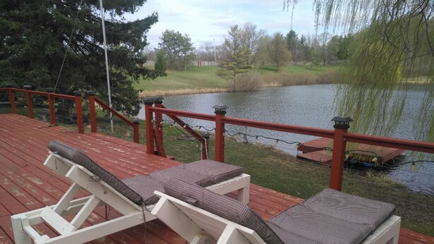 Une terrasse dotée de deux chaises longues blanches et d’une rambarde rouge, donnant sur un lac.