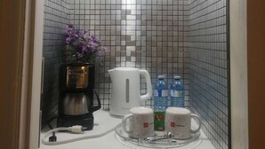 Une petite kitchenette équipée d’une machine à café, de deux tasses et d’une bouilloire, le tout posé sur un plan de travail.