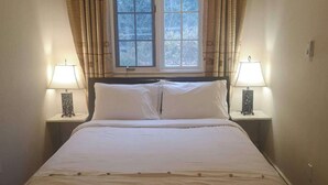 Une chambre à coucher avec un lit, deux tables de chevet avec des lampes, une fenêtre avec des rideaux et un plancher en bois.