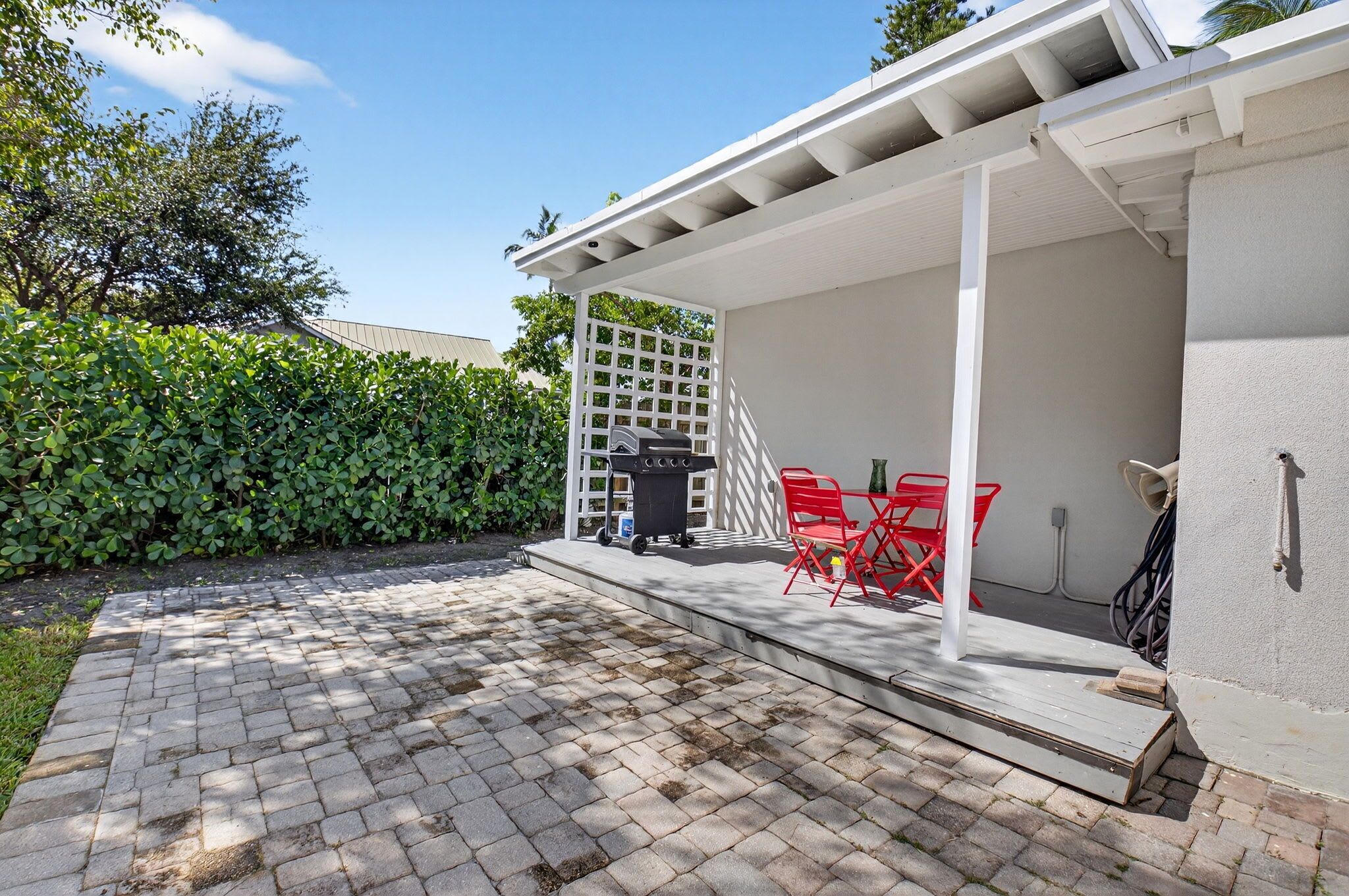 A patio area with a covered seating area, a grill, and a white fence.