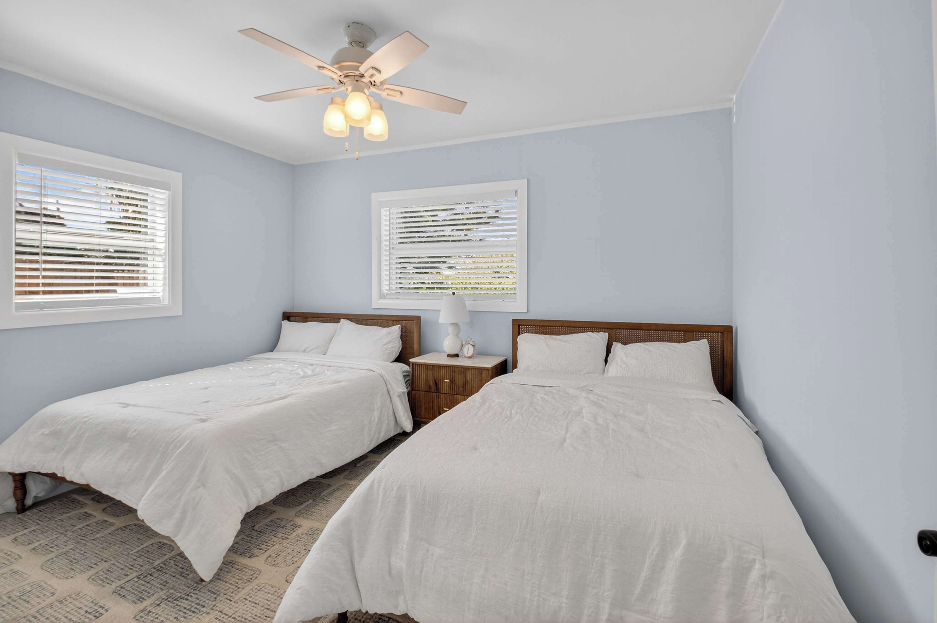 A bedroom with two single beds, a ceiling fan, and two bedside tables with lamps.
