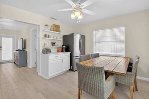 A modern kitchen with white cabinets, a stainless steel refrigerator, a coffee maker, and a dining table with wicker chairs. - Delray Daydream, Home for 8 (Delray Beach)