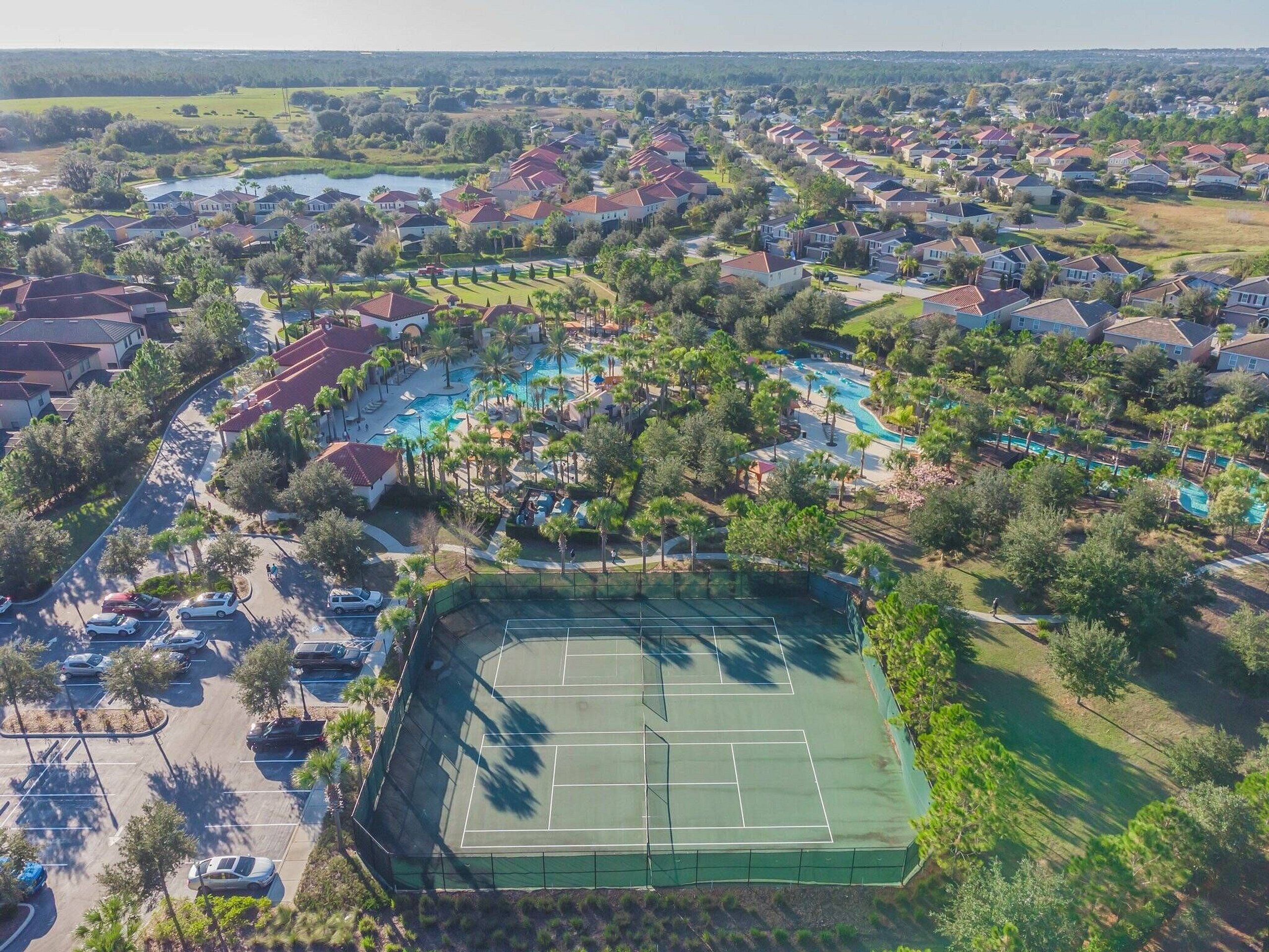 An aerial view of a residential area with a large swimming pool complex surrounded by houses and a tennis court.