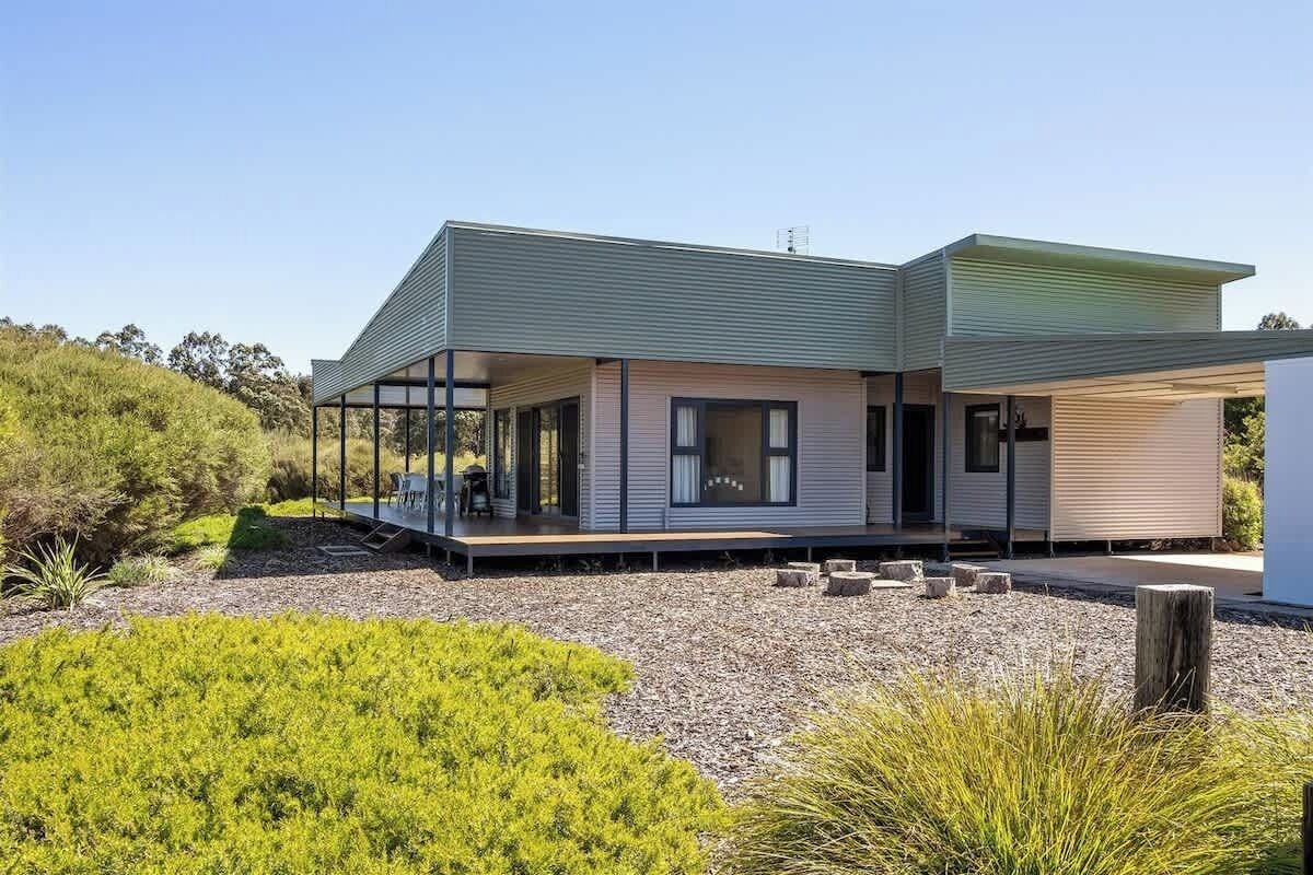 A modern two-story house with a covered outdoor area and a gravel driveway.
