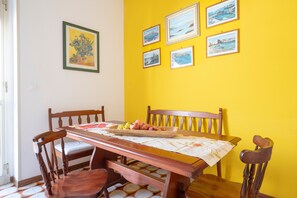 Un comedor con una mesa de madera, sillas y una pared amarilla con cuadros.