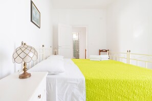 Una habitación con una cama, una mesita de noche, una lámpara y una puerta que da a otra estancia.