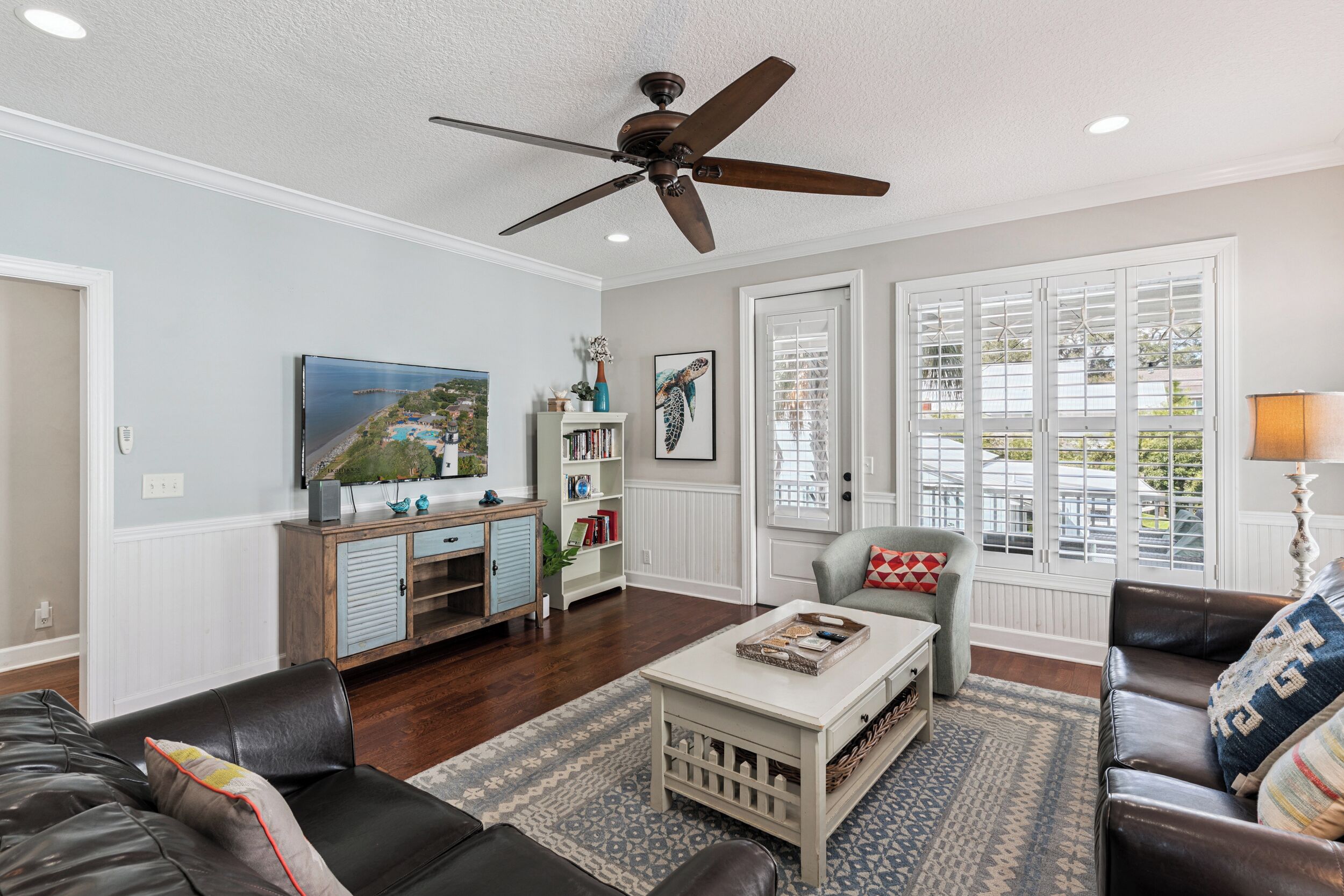 A living room with a ceiling fan, a coffee table, a sofa, a bookshelf, and a window with blinds.