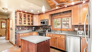 A modern kitchen with wooden cabinets, a central island, stainless steel appliances, and a stone backsplash. - Spacious House with Excellent Ski Area Views (Breckenridge)