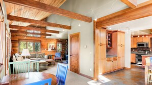 A spacious living area with a wooden ceiling, a dining table with blue chairs, and a kitchen with wooden cabinets and a microwave. - Spacious House with Excellent Ski Area Views (Breckenridge)