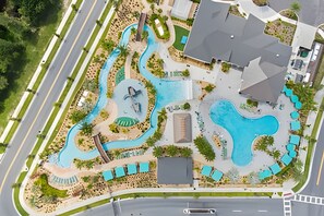 An aerial view of a resort with multiple swimming pools, a central building, and a road running alongside. - Storey Lake 2BR Condo — Lake & Clubhouse View (Kissimmee)