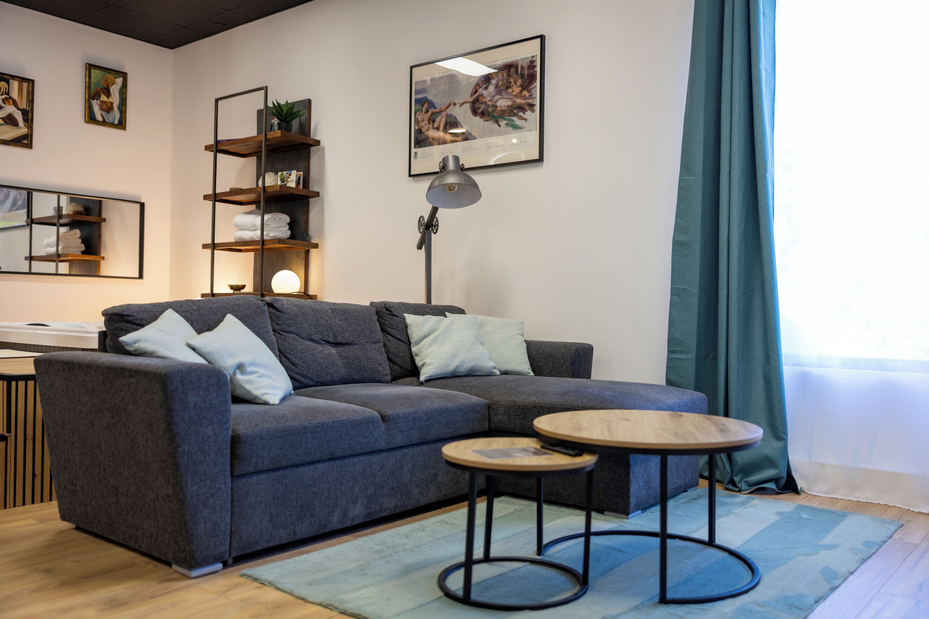 Un salon moderne avec un canapé gris, une petite table ronde, une lampe sur pied et une bibliothèque.