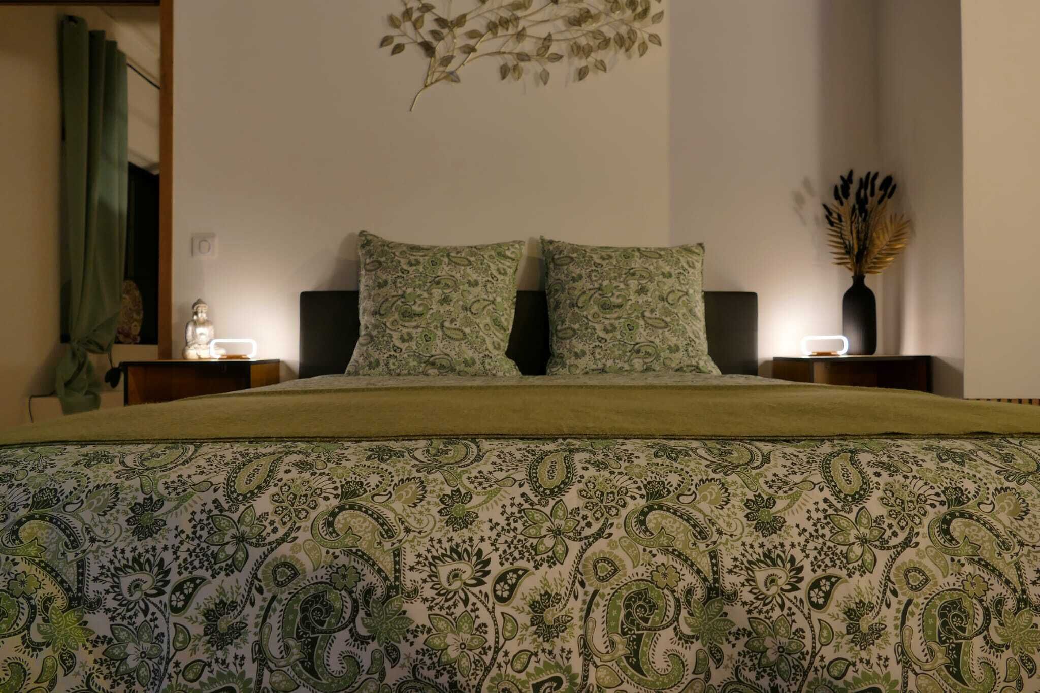 Une chambre à coucher avec un lit, deux tables de chevet, une plante fixée au mur et un rideau vert.
