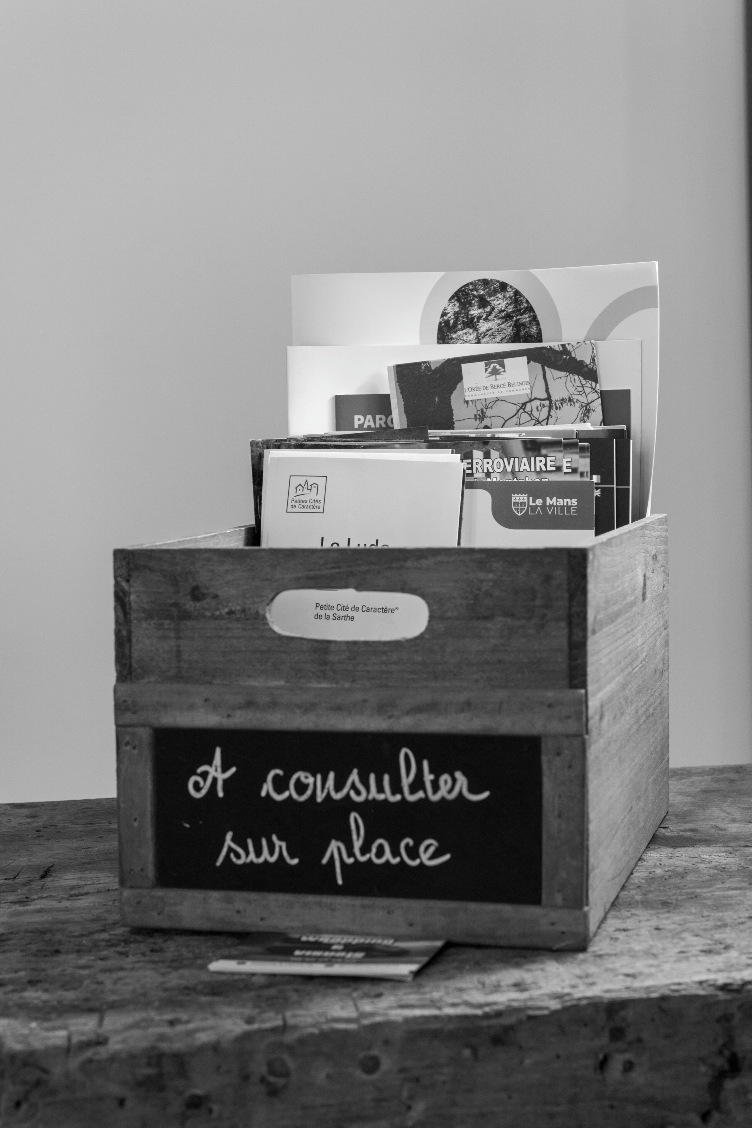 Une caisse en bois portant une étiquette indiquant « À consulter sur place » et contenant divers livres et magazines.