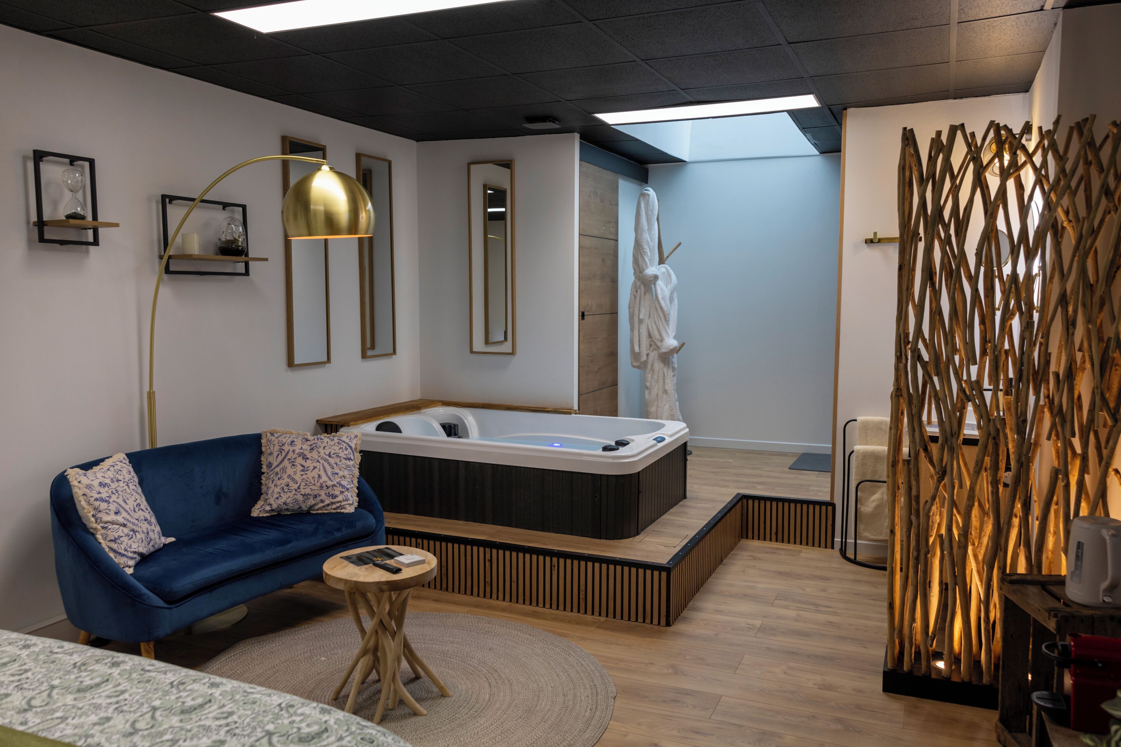 Una camera moderna con un divano blu, un tavolino rotondo in legno, una vasca idromassaggio e un pannello decorativo in legno.