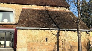 A rustic building with a sloped roof, a large window, and a stone wall. - Château de Posset - Les lofts (Teloché)