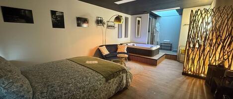 A modern room with a bed, a sofa, a small table, and a decorative partition.