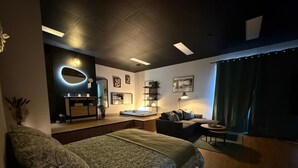 Una moderna camera d'albergo con un letto, una zona salotto con divano e poltrone, una toeletta con specchio e un tavolino.