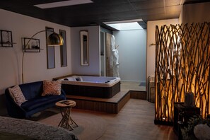Una habitación moderna con sofá, una mesita redonda, un jacuzzi y un adornado en la pared.