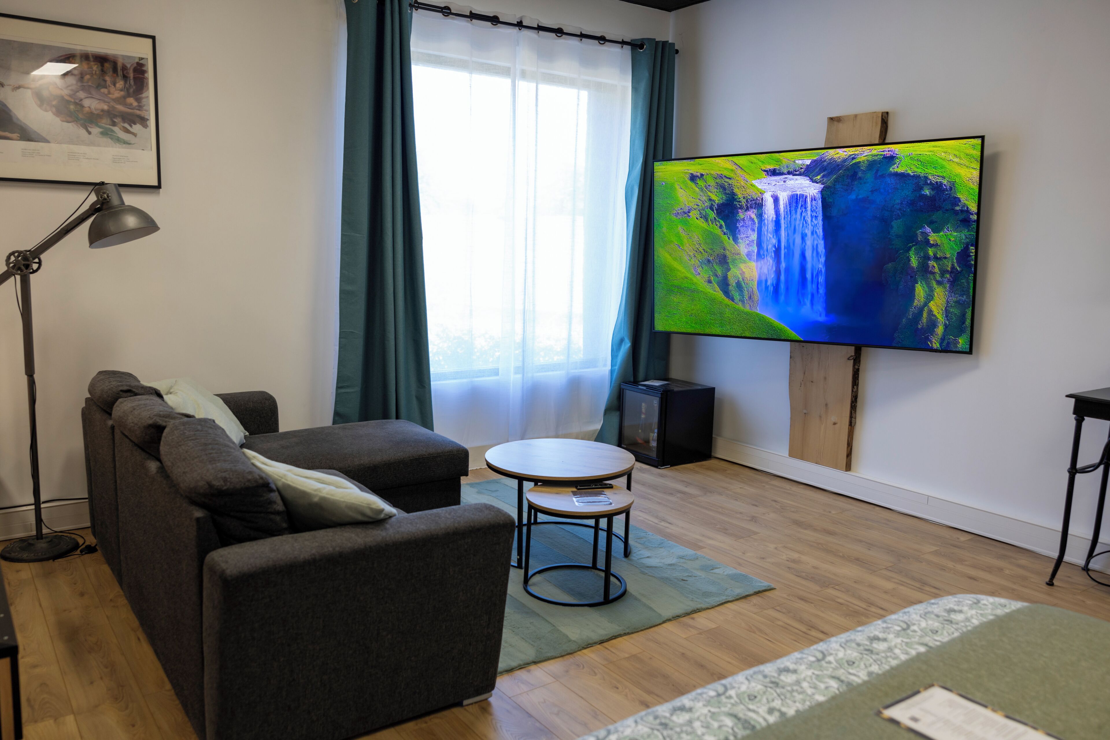 A living room with a sofa, a small table, a TV, a lamp, and a window with curtains.