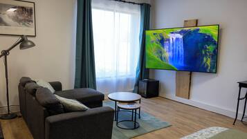 A living room with a sofa, a small table, a TV, a lamp, and a window with curtains.