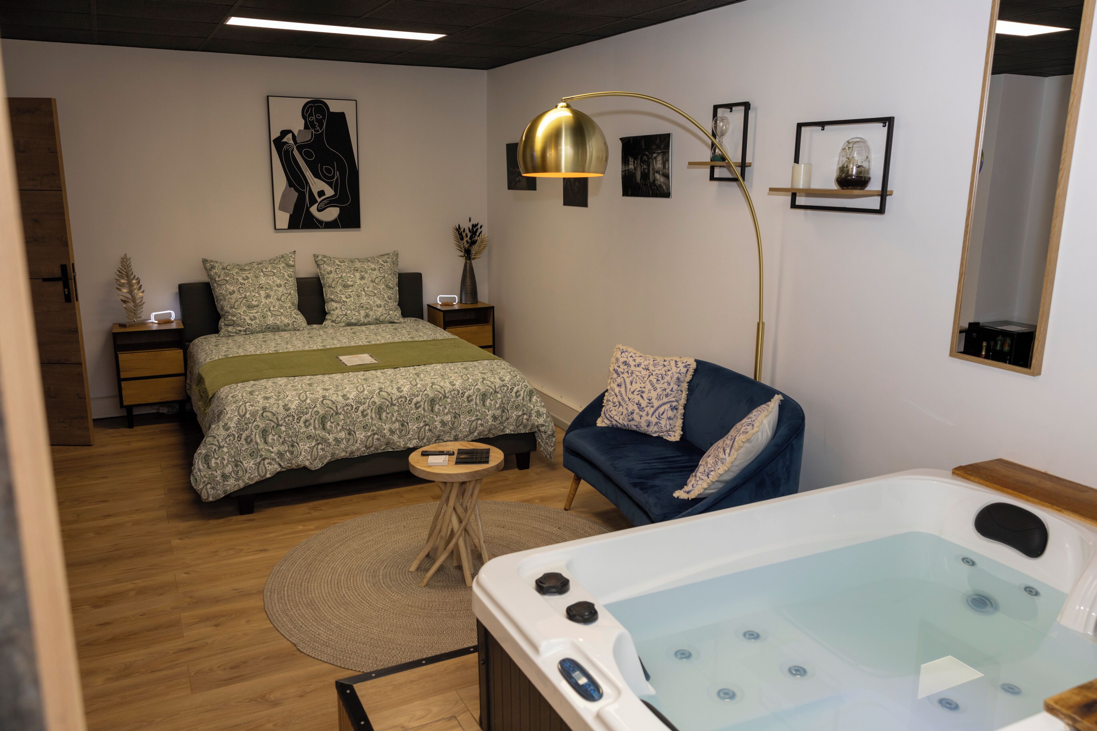 Een slaapkamer met een bed, een stoel, een nachtkastje, een bijzettafeltje, een lamp, een spiegel en een bubbelbad.