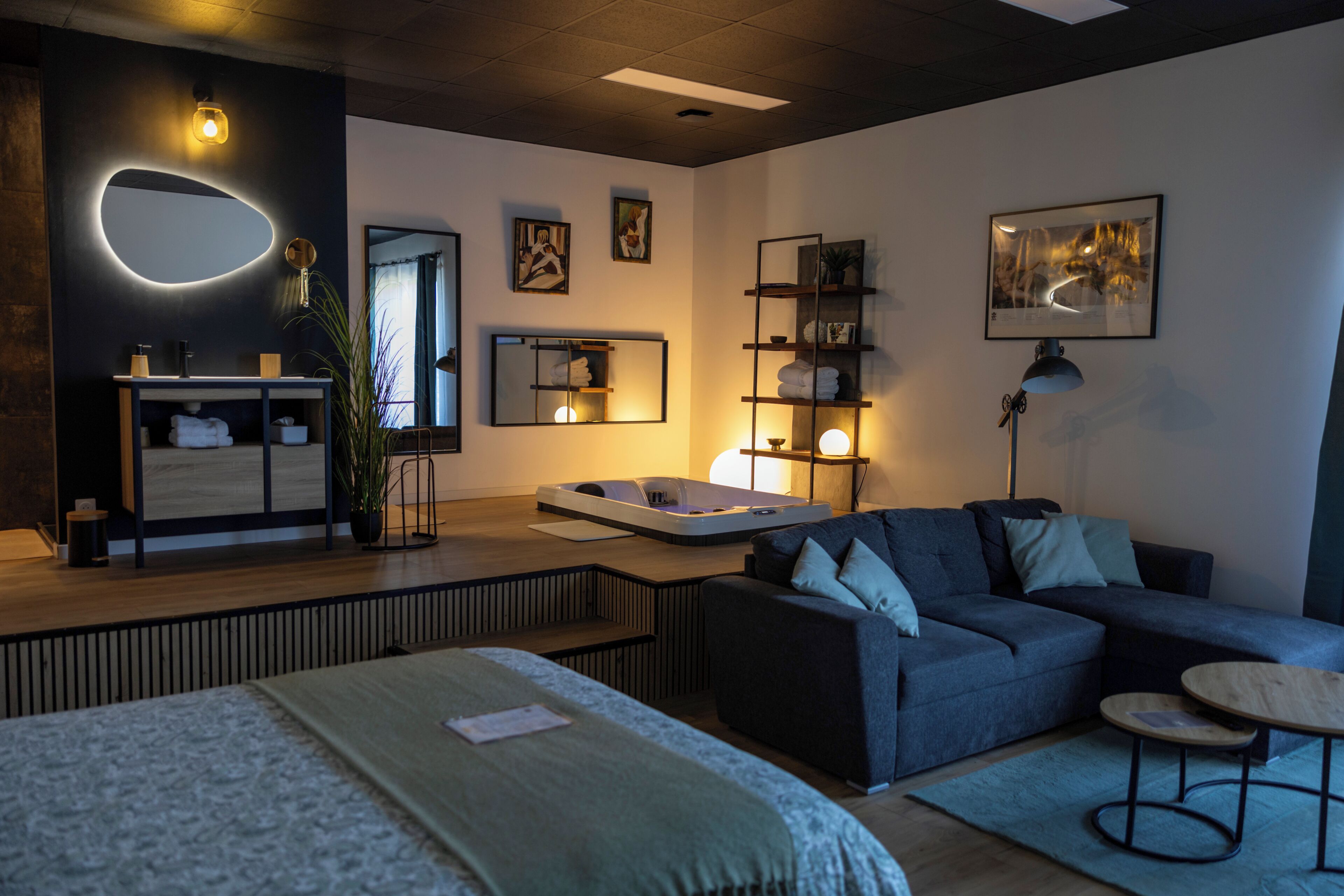 A modern living room with a sofa, a small table, a bed, and a bathroom with a mirror and sink.