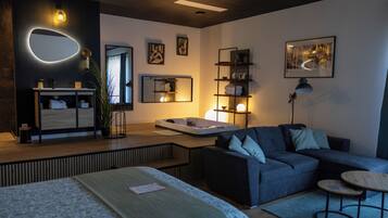 A modern living room with a sofa, a small table, a bed, and a bathroom with a mirror and sink.