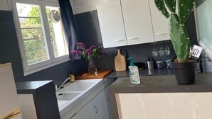 Una cocina con un lavamanos, una ventana con cortinas, una planta de cactus y una tabla de cortar de madera.