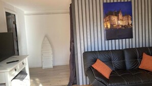 Una sala de estar con un sofá de cuero negro, un televisor sobre un mueble blanco y un cuadro de un castillo en la pared.
