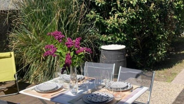 Juego de mesa exterior con vajilla de vidrio transparente, platos y un florero con flores moradas.